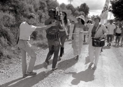 A group of people walk down a road while being filmed.