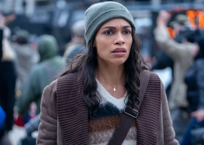 Rosario Dawson as Alma wearing a jacket and beanie looking distraught in a crowded New York.